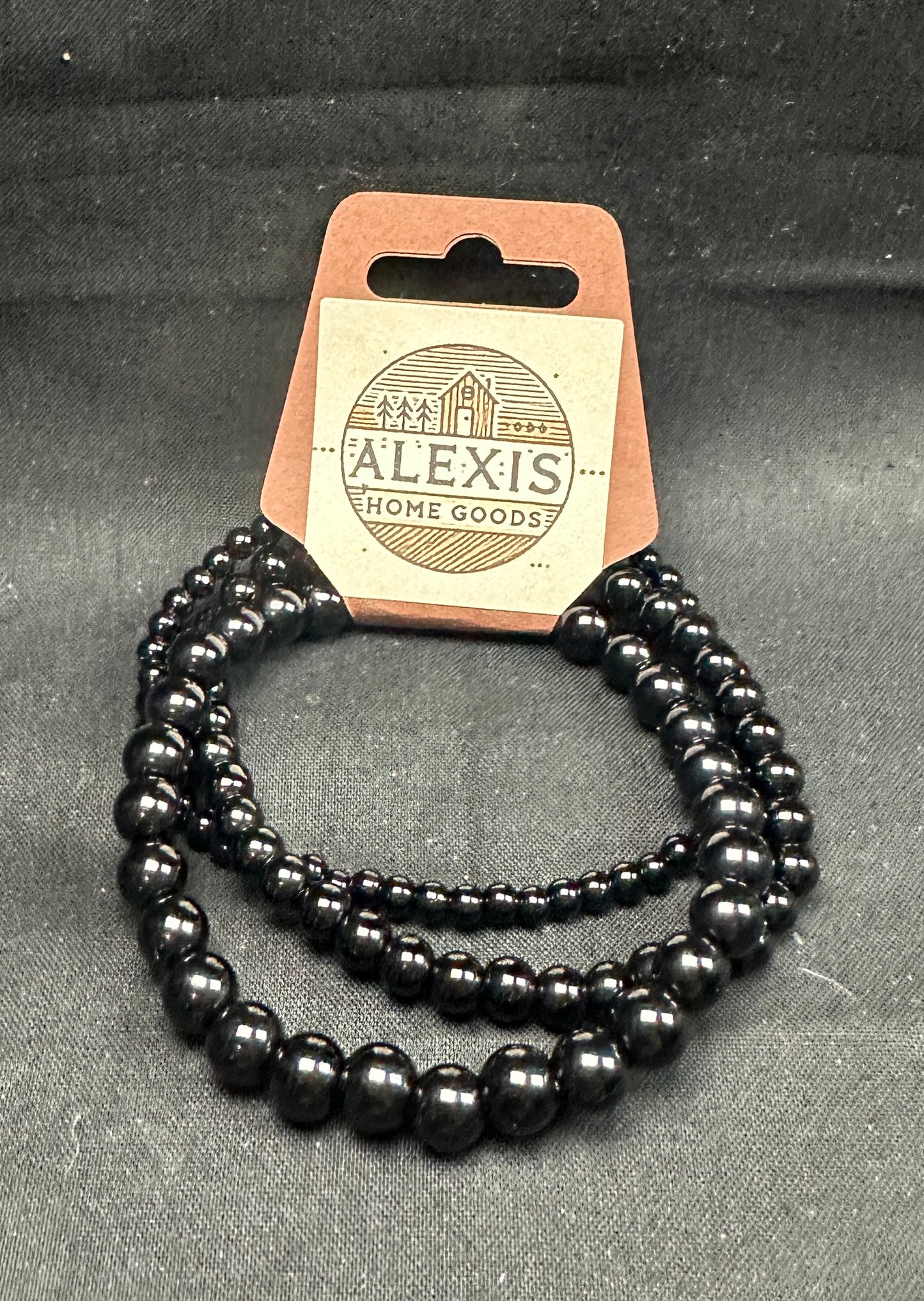 Close-up image of a 3-pack black onyx bracelet set from Alexis Home Goods, featuring beads in 4mm, 6mm, and 8mm sizes. Each bracelet highlights the sleek, polished jet-black finish of onyx stones, symbolizing protection and strength. The stretchy design ensures a comfortable fit for most wrist sizes.