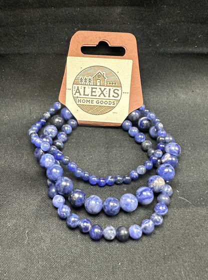 Close-up image of a 3-pack blue sodalite bracelet set from Alexis Home Goods, featuring beads in 4mm, 6mm, and 8mm sizes. Each bracelet highlights the deep blue tones with natural white veining of sodalite stones, known for inspiring clarity, intuition, and emotional balance. The stretchy design ensures a comfortable fit for most wrist sizes