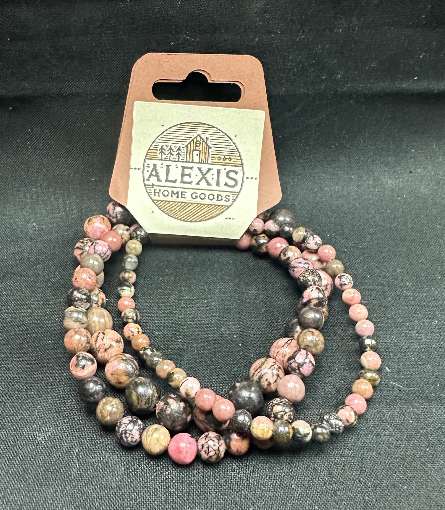 Close-up image of a 3-pack rhodonite bracelet set from Alexis Home Goods, featuring beads in 4mm, 6mm, and 8mm sizes. Each bracelet displays the rosy pink tones and natural black veining of rhodonite stones, celebrated for promoting emotional balance and healing. The stretchy design ensures a comfortable fit for most wrist sizes.